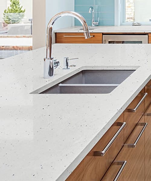 Speckled white granite countertop with an undermount sink over walnut drawers